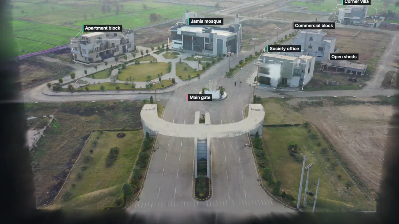 The entrance of a housing society in 3D: an arched gate, a roundabout, a park, a mosque, flats, an office, a grey-structure block and sheds, each outlined and labelled